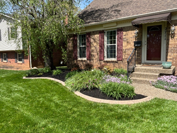 A brick house with a well-manicured lawn and a flower bed filled with plants.
