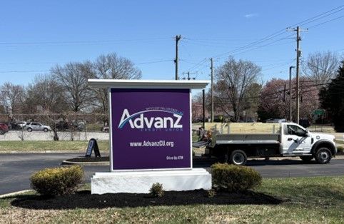 A white truck is parked in front of a purple advanz sign.