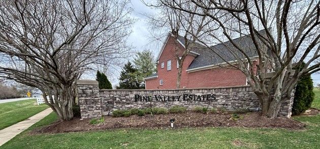 A stone wall with a sign in front of a brick house.