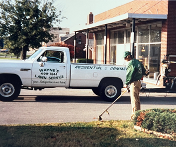 A man is mowing a lawn in front of a truck that says wayne 's lawn service