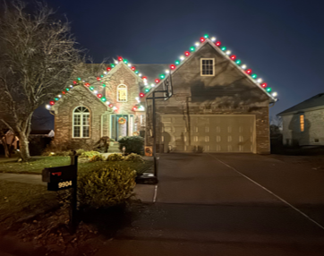 House at night outlined with red and green holiday lights, with a lit driveway and mailbox in front. House at night outlined with red and green holiday lights, with a lit driveway and mailbox in front.
