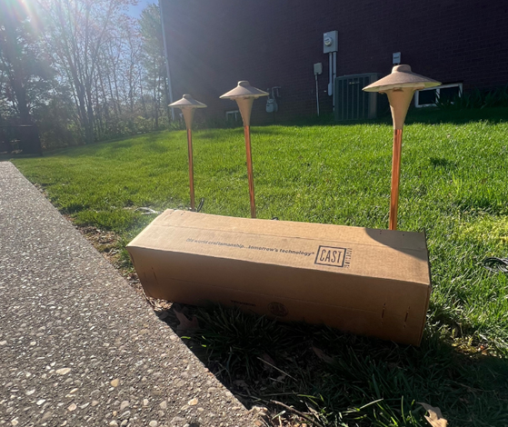 A cardboard box is sitting on the side of the road next to a grassy field.