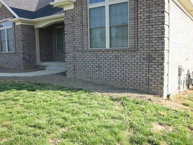 A brick house with a curved walkway and a patchy lawn in front. The house has light-colored trim around the windows.