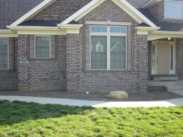 Brick house with windows, a front door, and a small lawn; the brick is a mix of gray and brown.