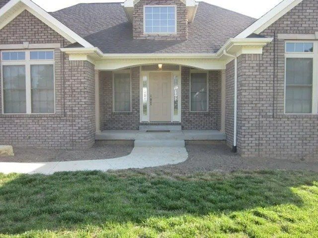 Brick house with a curved concrete walkway leading to the front door. Green lawn in the foreground.