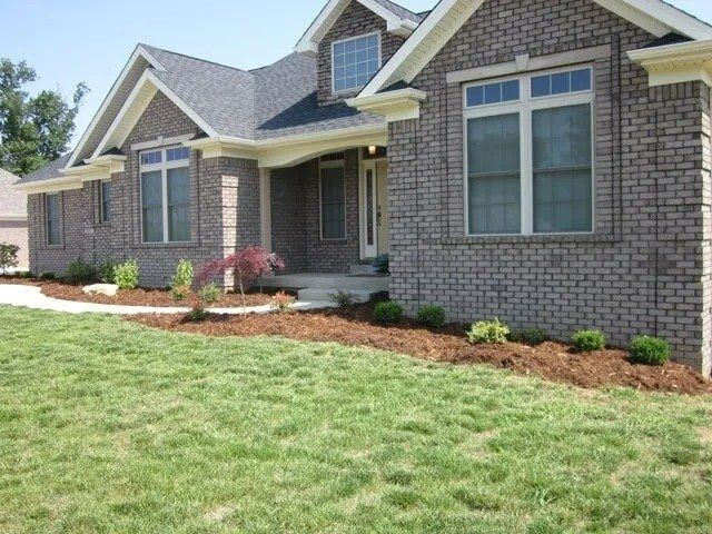 Brick house with green lawn and landscaped bed with mulch, shrubs, and small tree.
