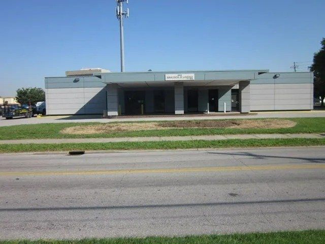 A single-story building with a covered entrance on a sunny day, set back from a road with grass in front.