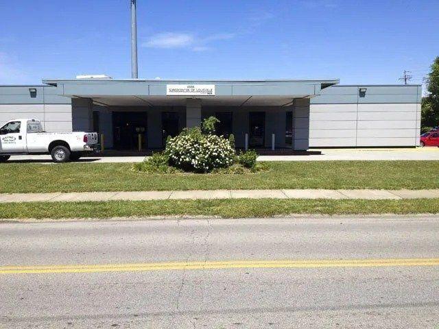 Exterior of the U.S. Post Office, a one-story building with a white truck parked nearby. Green grass and a small bush in front.