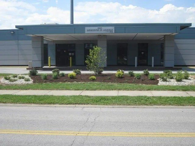 Building entrance with landscaping, small tree, and a sign that reads 