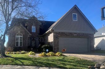 Brick and siding house with two-car garage, front lawn, and clear blue sky. Brick and siding house with two-car garage, front lawn, and clear blue sky.