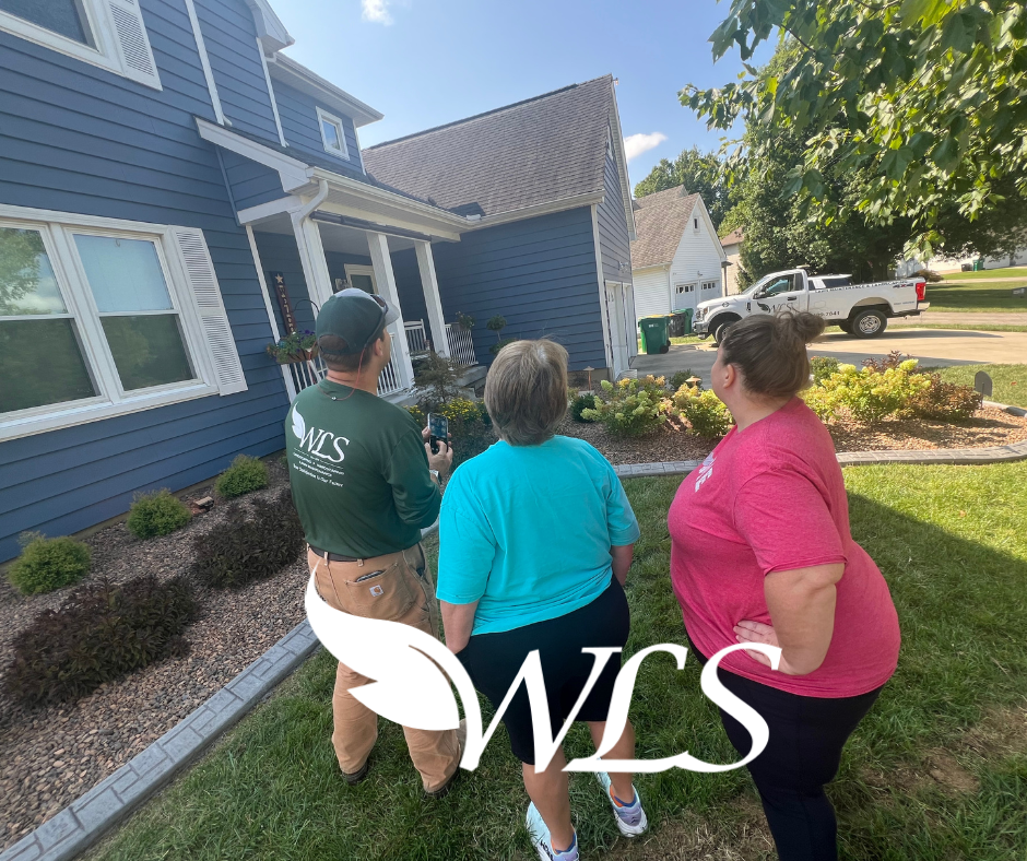 A man and two women are standing in front of a blue house.