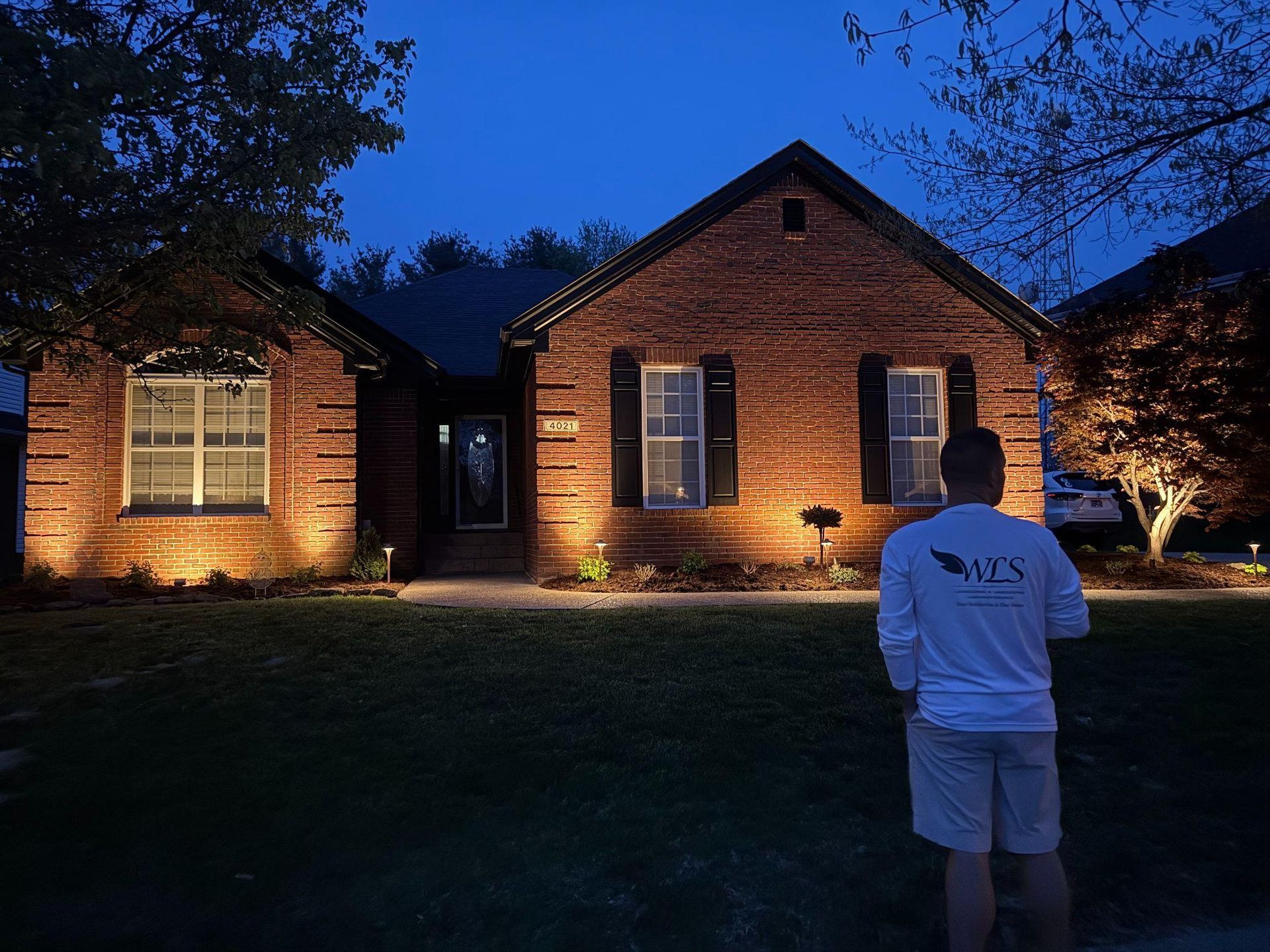 A man is standing in front of a brick house at night.