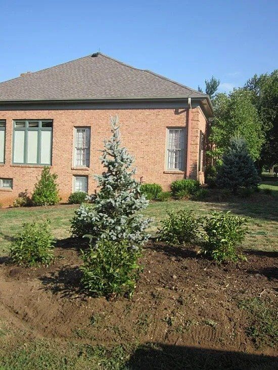 A brick house with a brown roof, surrounded by freshly tilled flowerbeds with new plants.