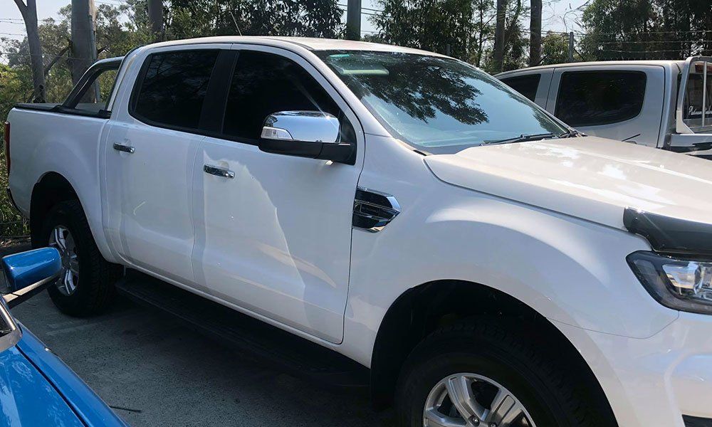A white truck is parked next to a blue truck in a parking lot.