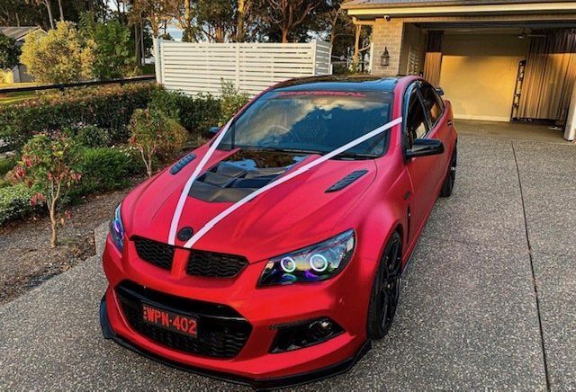 A red car with white ribbons on the hood is parked in front of a house.