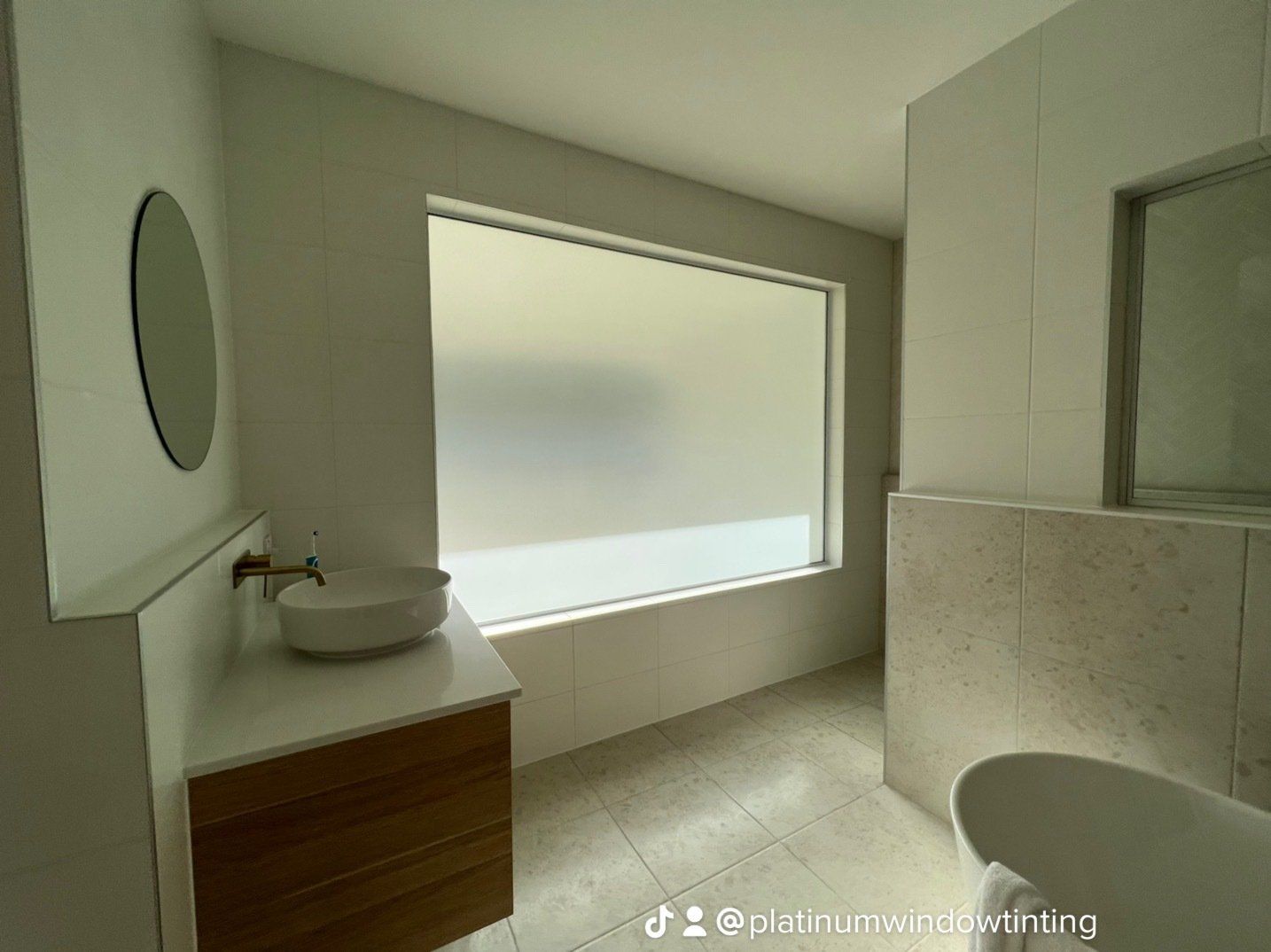 A bathroom with a sink , mirror , tub and large window.