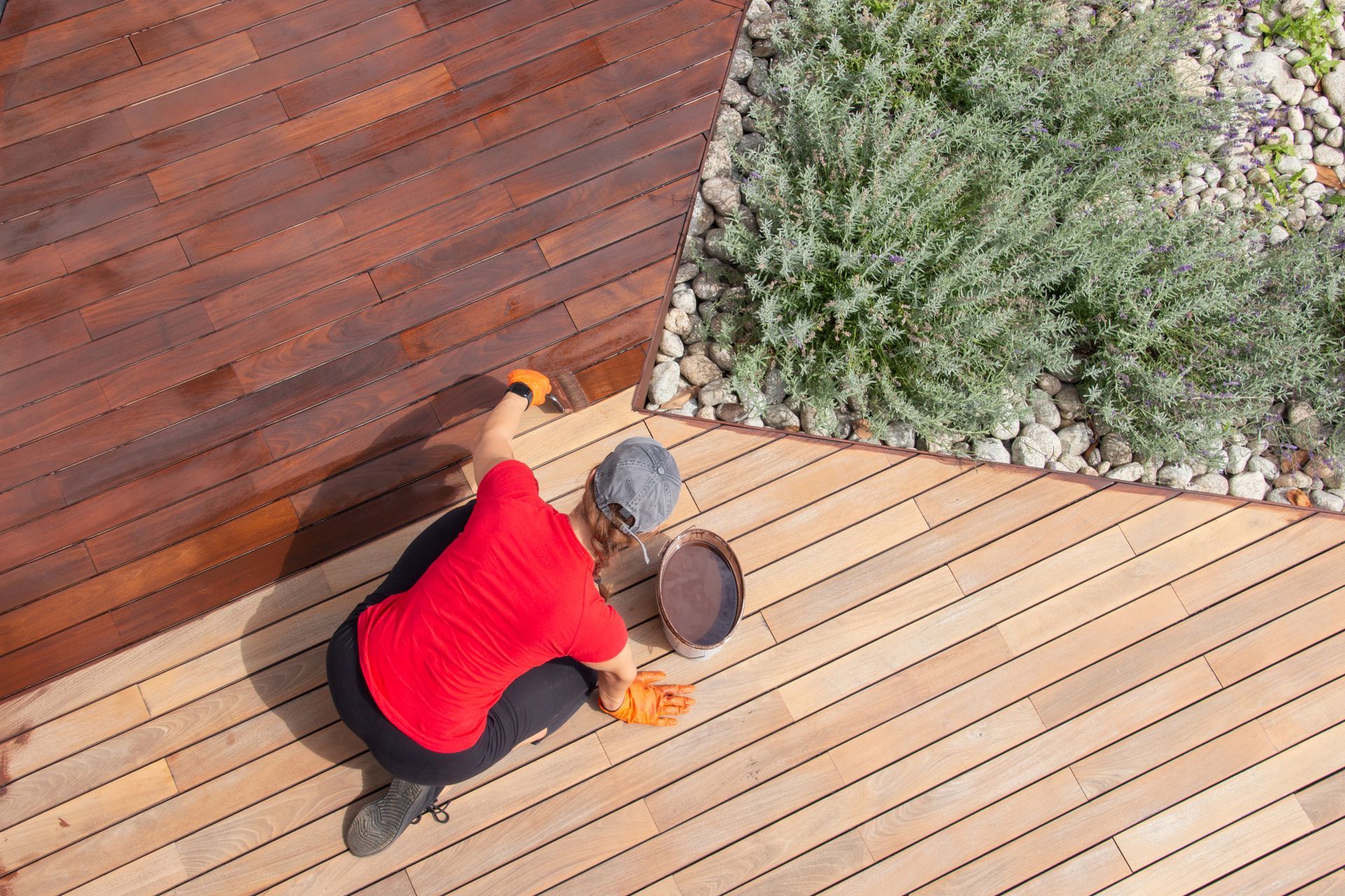 A man is kneeling on a wooden deck painting it.