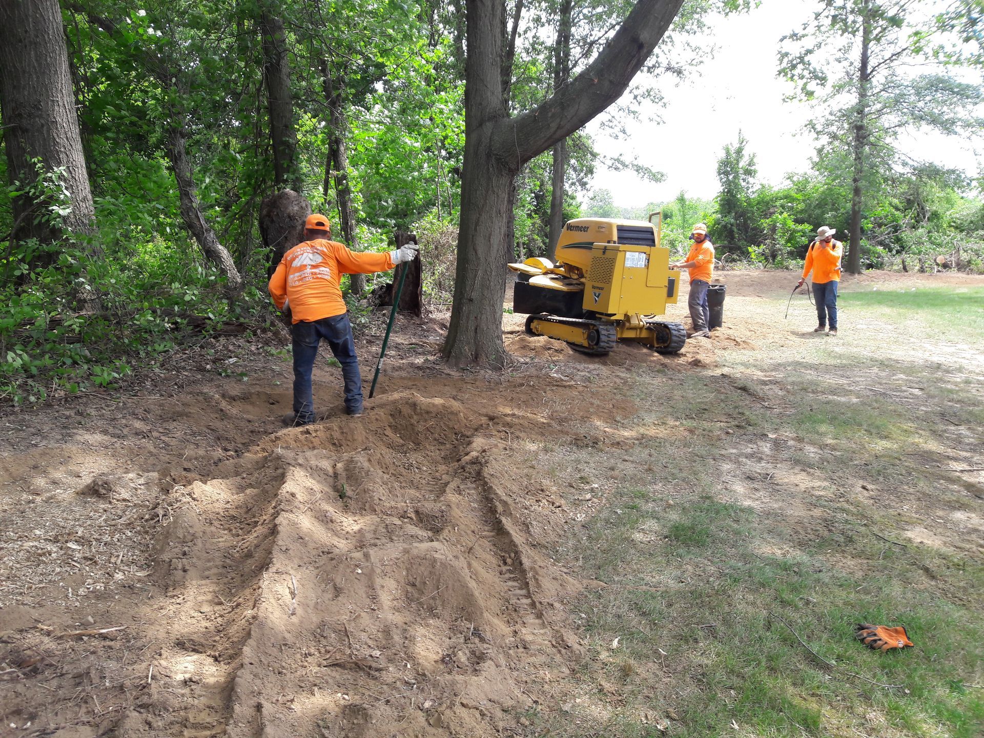 A group of men are working on a stump grinder in the woods.