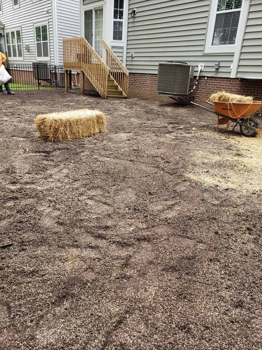 A bale of hay is sitting on top of a pile of dirt next to a wheelbarrow.