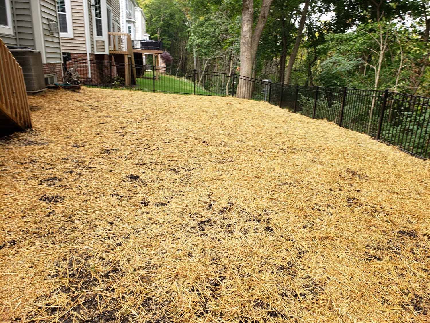 A large pile of wood chips in a backyard next to a house.
