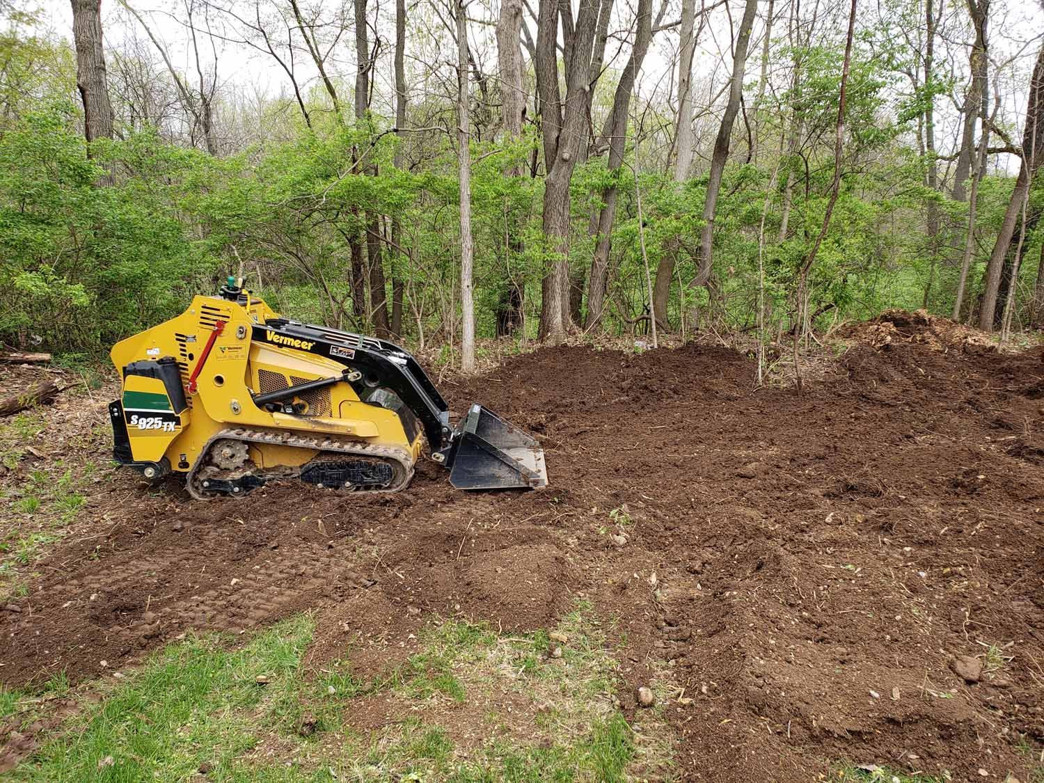 A bulldozer is sitting in the middle of a dirt field in the woods.