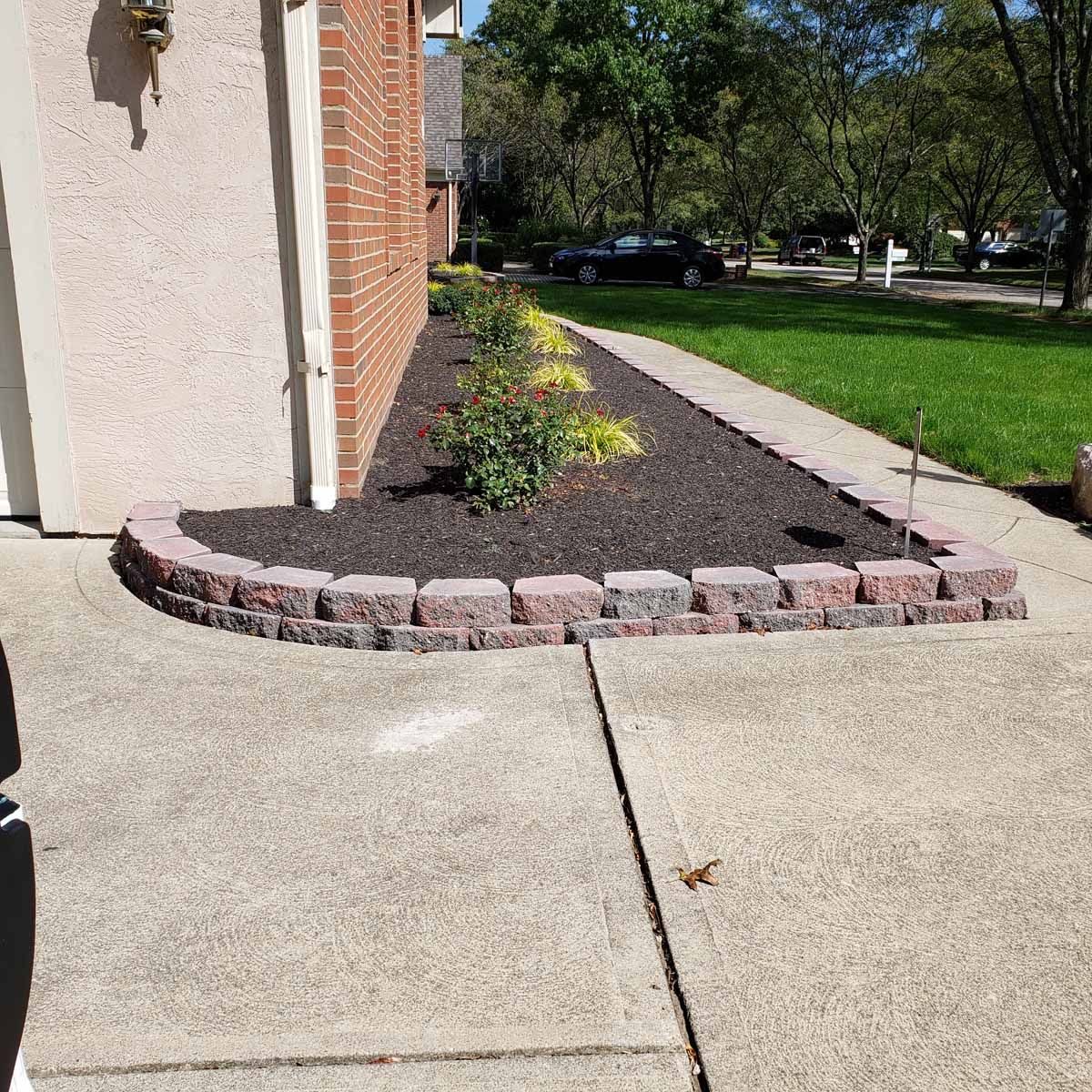 A brick walkway leading to a house with a garden in front of it.