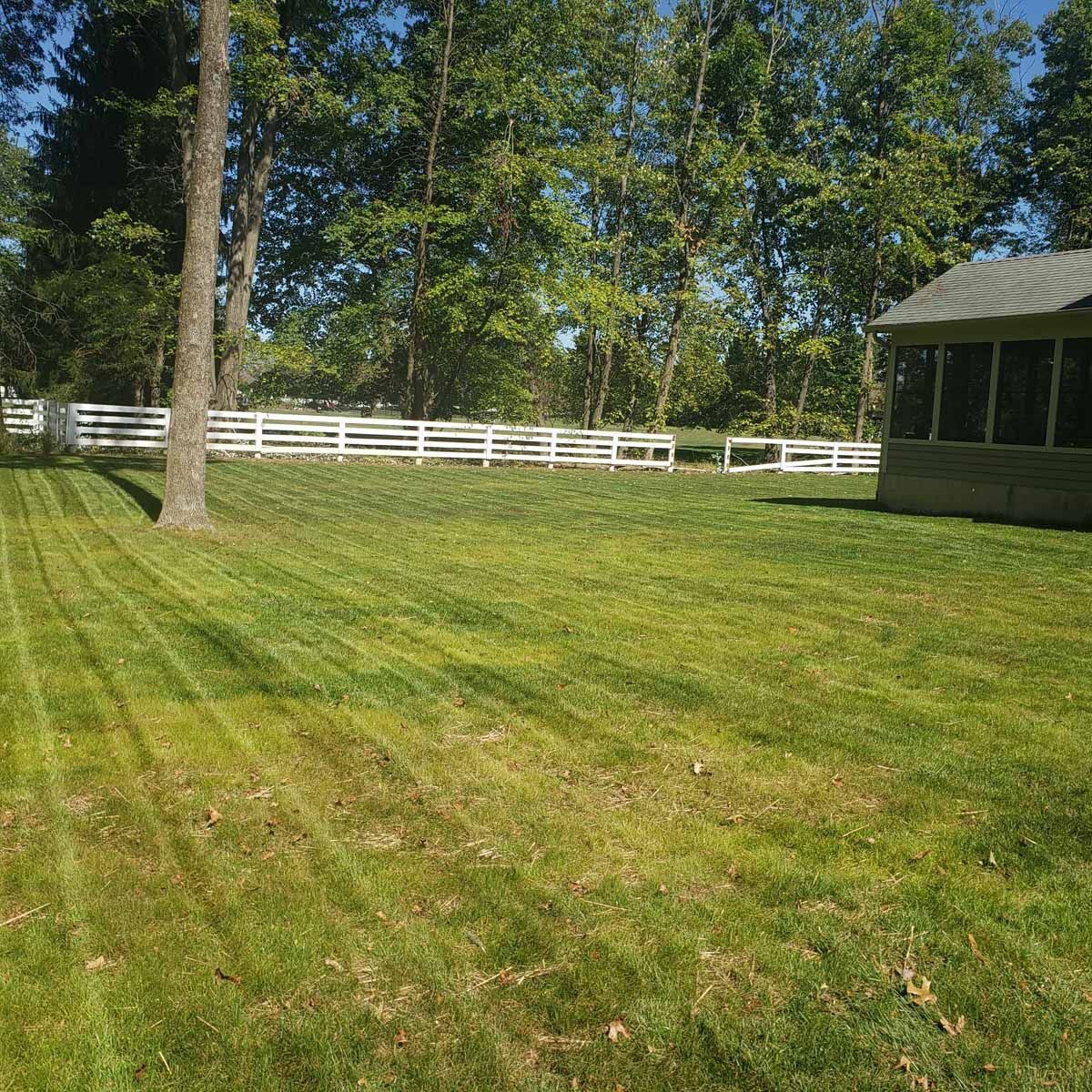 A lush green lawn with a white fence and a screened in porch.