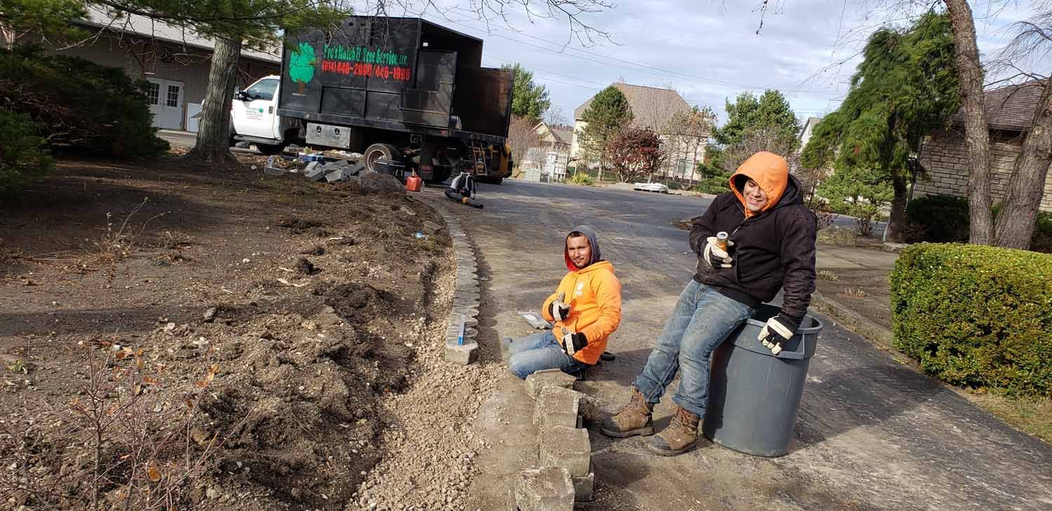 Two men are kneeling down next to a trash can on the side of the road.