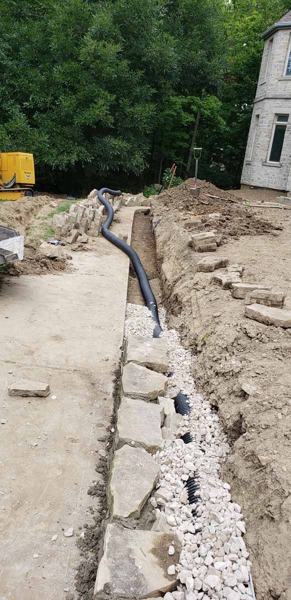 A drain pipe is being installed in the dirt next to a stone wall.