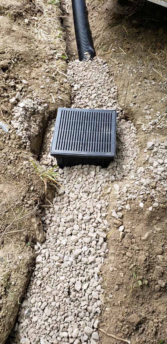 A black drain cover is sitting on top of a pile of gravel.