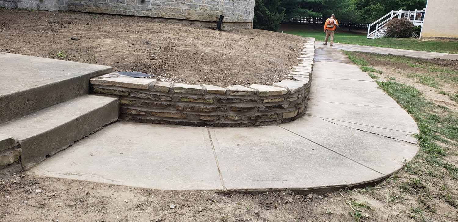 A person is walking down a sidewalk next to a stone wall.