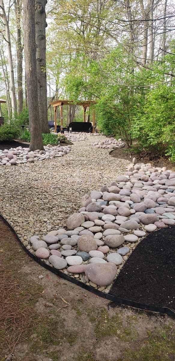 A path lined with rocks and gravel leading to a gazebo in the woods.