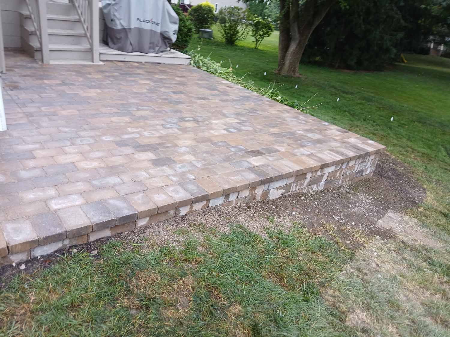 A brick patio is being built in the backyard of a house.
