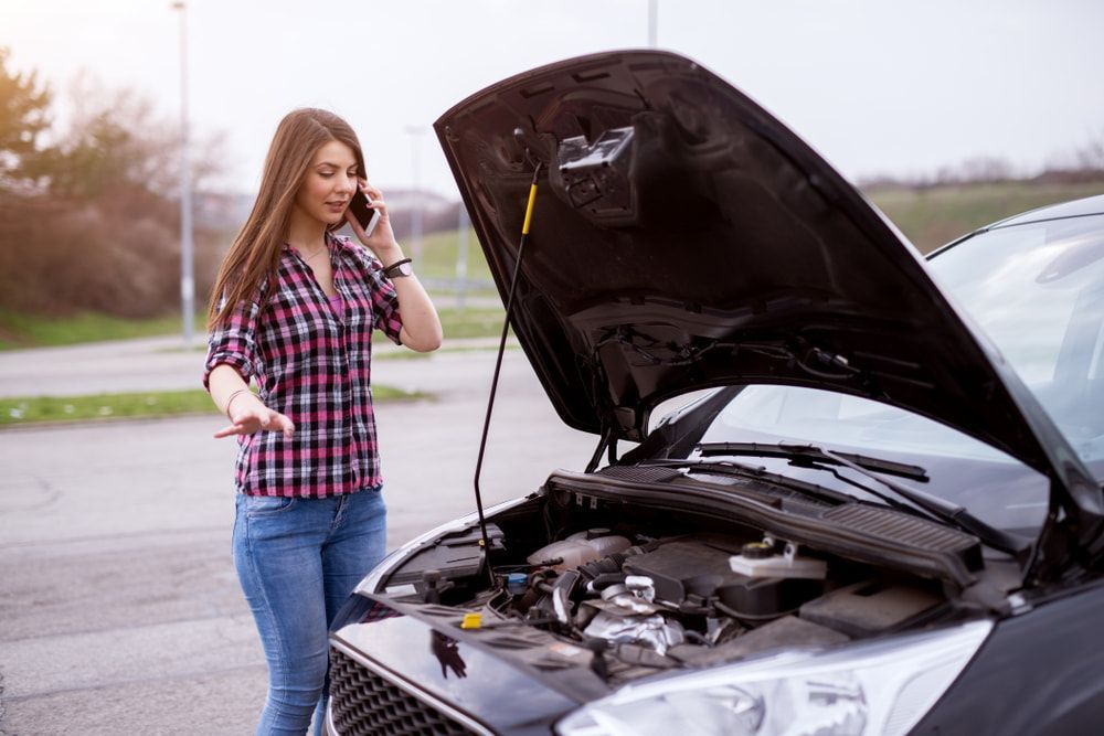 Woman standing beside a car with the bonnet open speaking on her phone