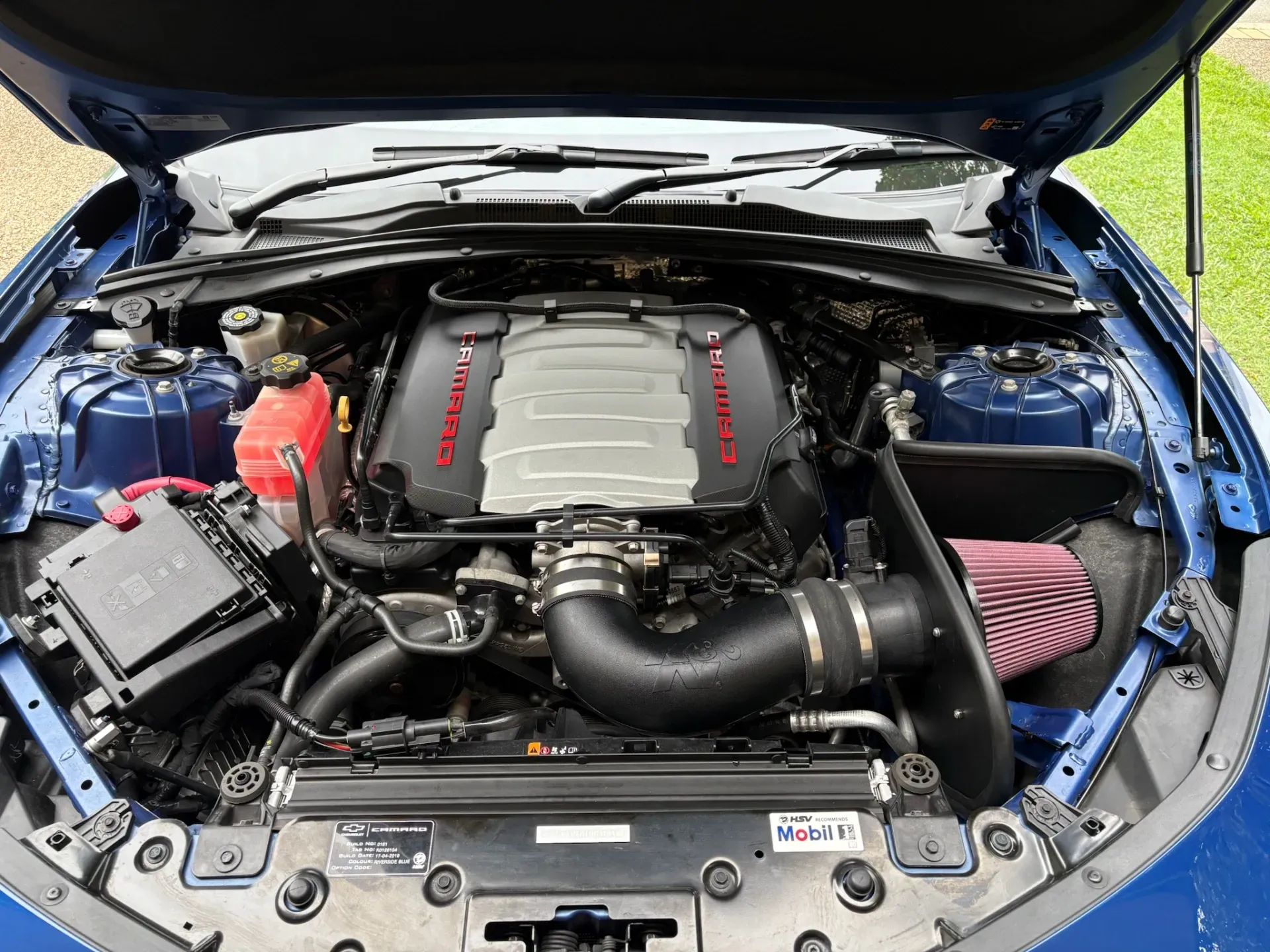Blue car engine bay with black components, air intake, and red lettering.