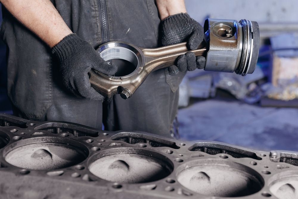 Mechanic holding a piston and connecting rod, working on an engine block in a garage. — Prime Mobile Mechanics in Varsity Lakes, QLD