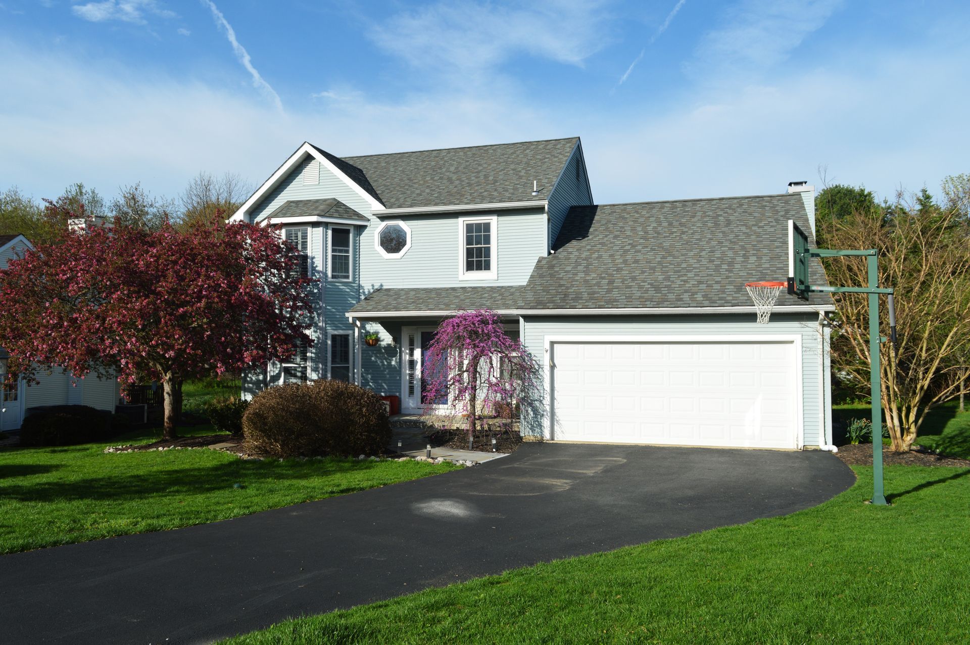 Blue two-story house with white garage door and basketball hoop in front, set on a green lawn.