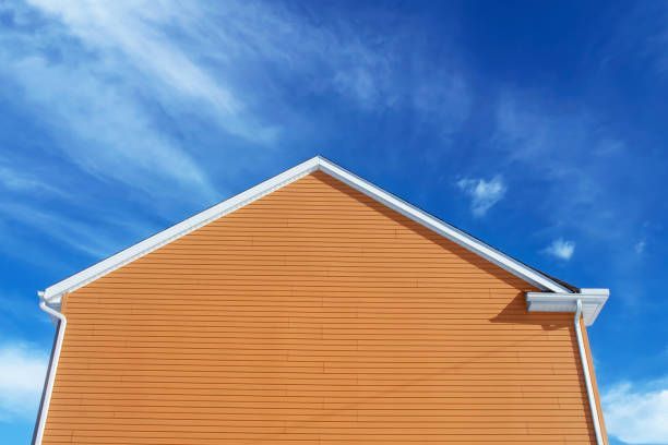 Orange house siding against a bright blue sky with wispy clouds.