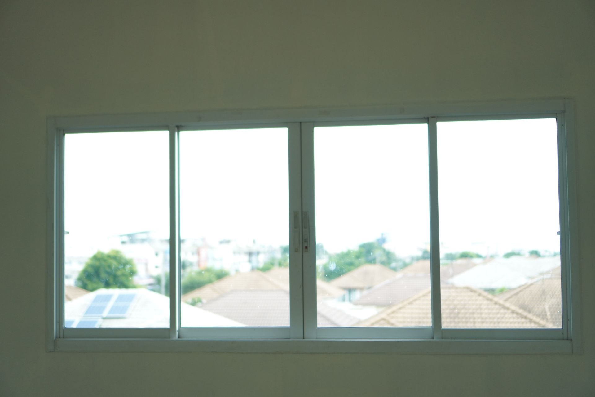 Sliding glass window with view of rooftops and cloudy sky.