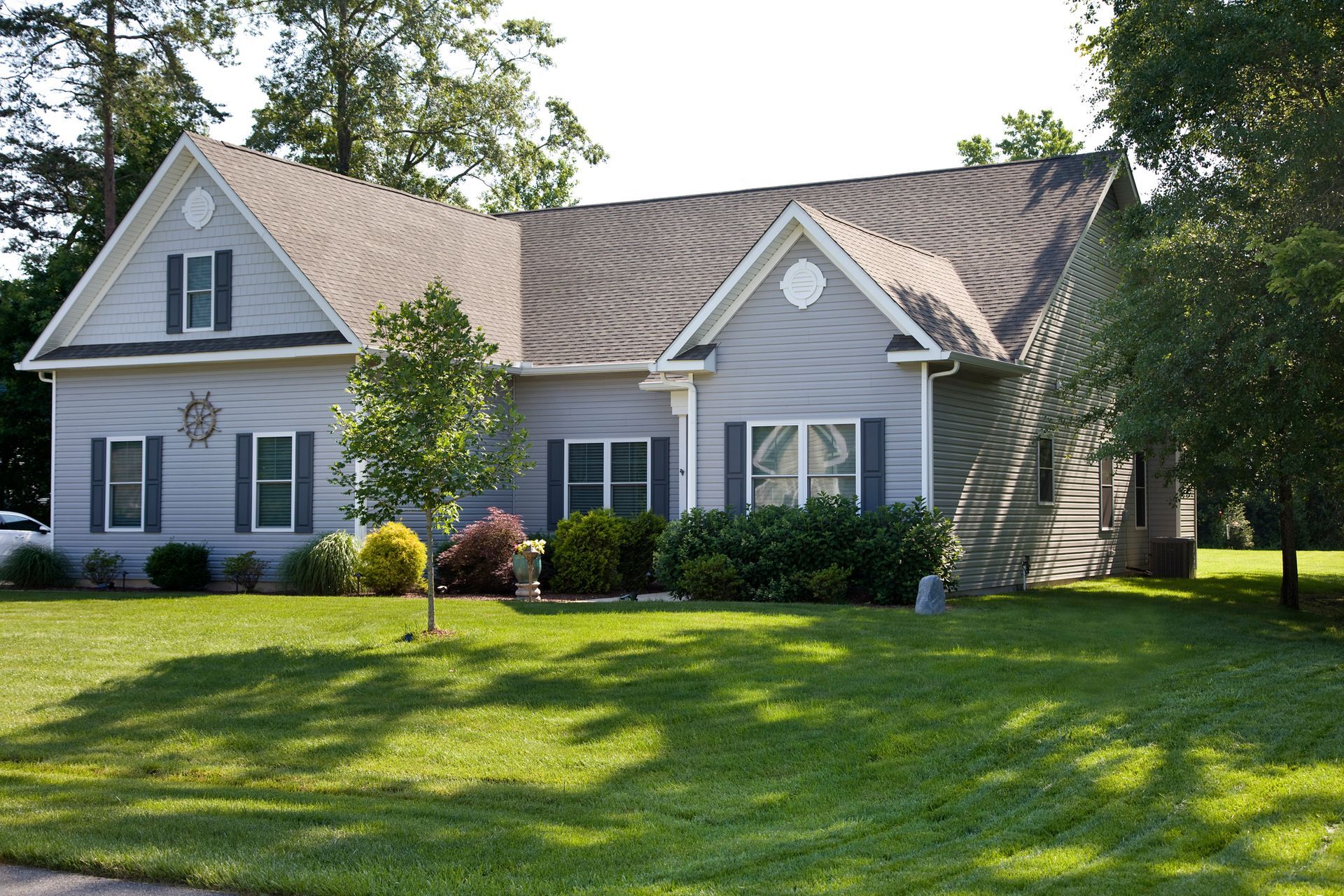 Gray house with dark shutters and roof, set on a green lawn with trees.