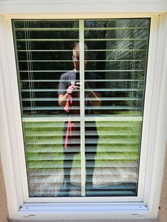 A man is taking a picture of himself in a window with blinds.