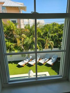 A view of a backyard through a window with lawn chairs and palm trees.