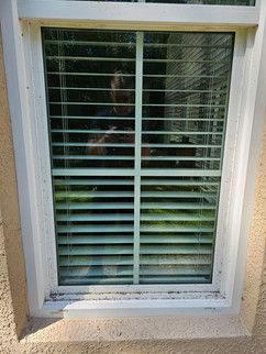 A man is taking a picture of himself in a window with blinds.
