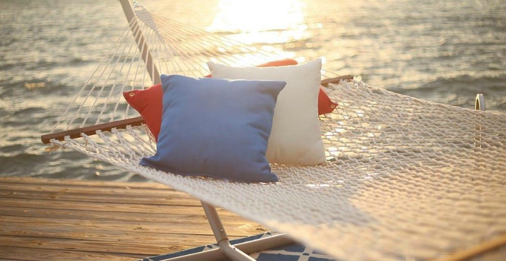 Hammock with pillows on a wooden dock overlooking water at sunset.