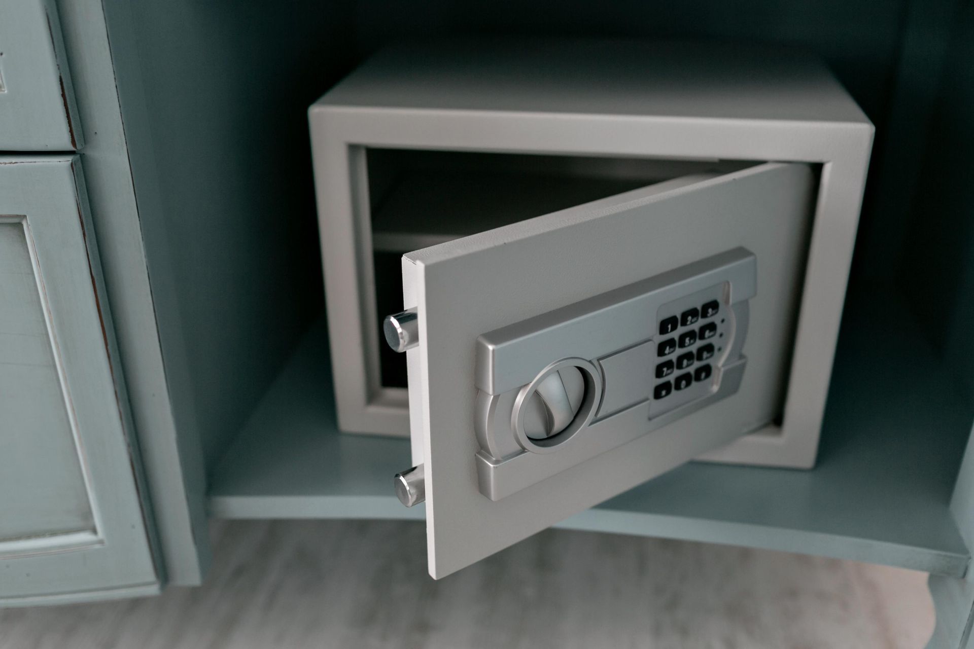 Gray open safe in a light blue cabinet. The safe has a keypad and a circular handle.
