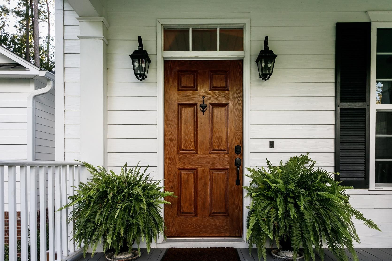 Wooden front door with ferns, black lamps, and white siding.