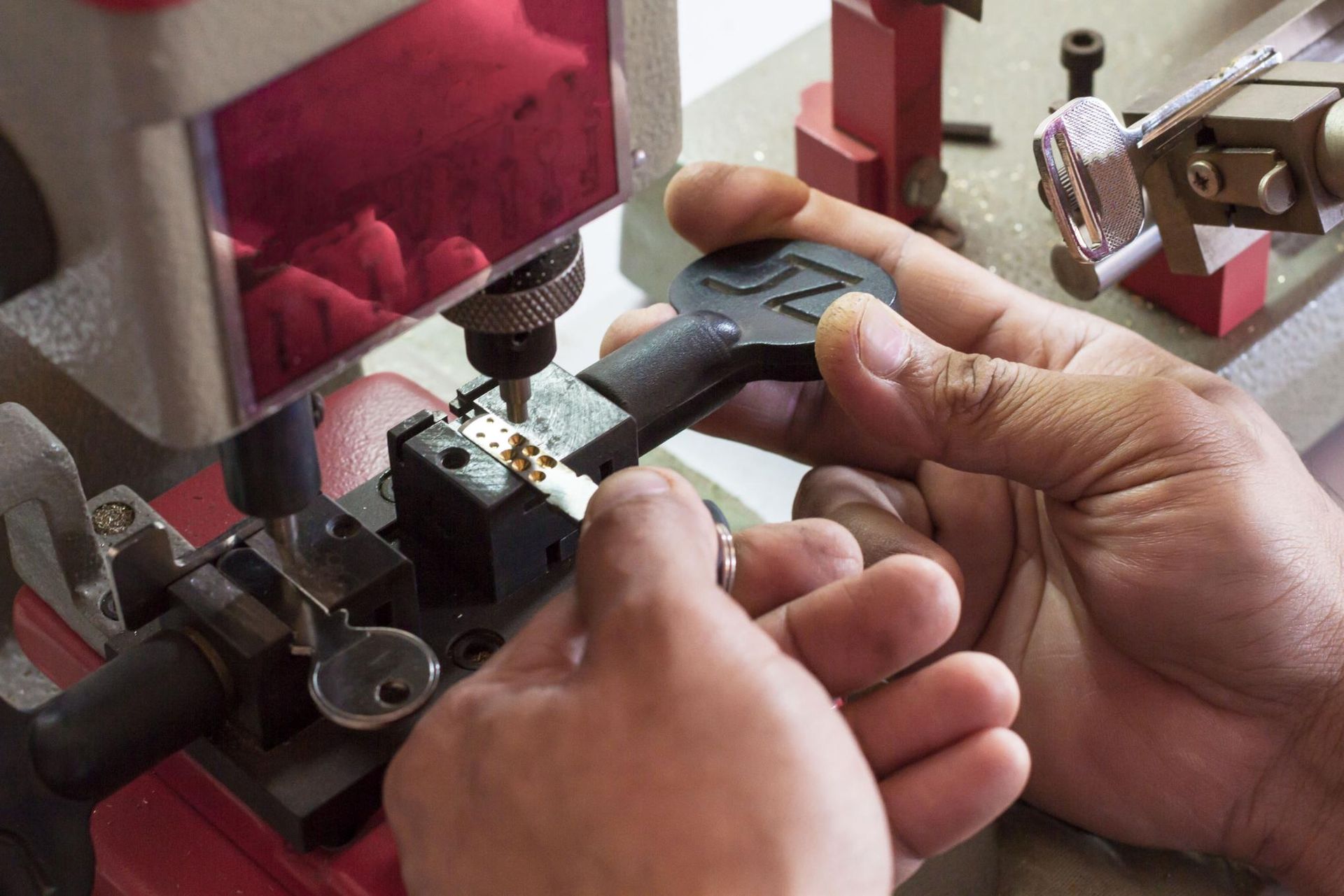 Person cutting a key on a key-cutting machine. The key is in a clamp, and the machine has a blade.