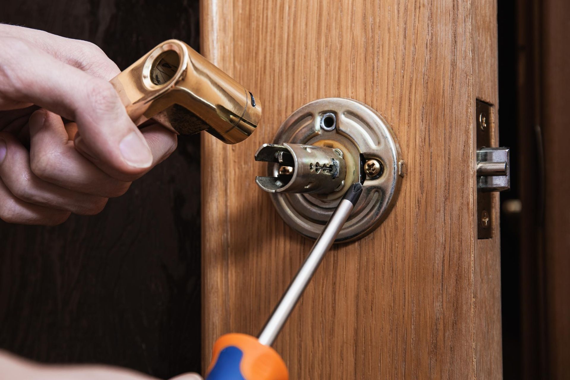 Person using a screwdriver to install a brass door handle on a wooden door.