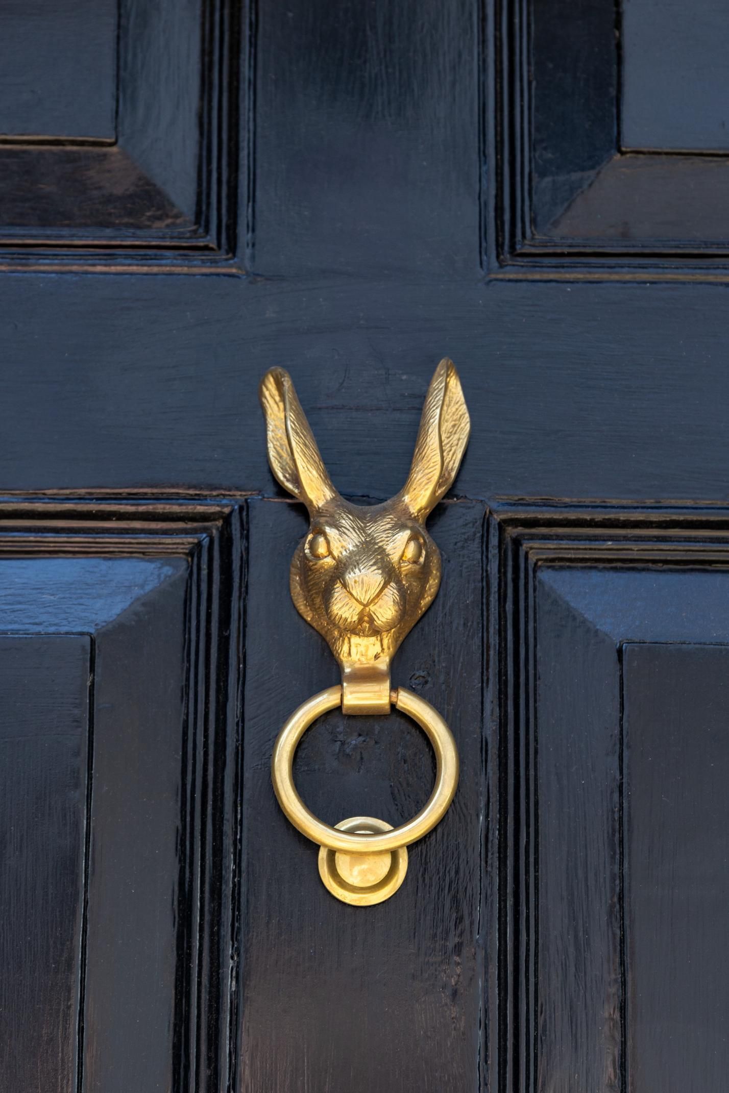 Gold bunny-shaped door knocker on a black paneled door.