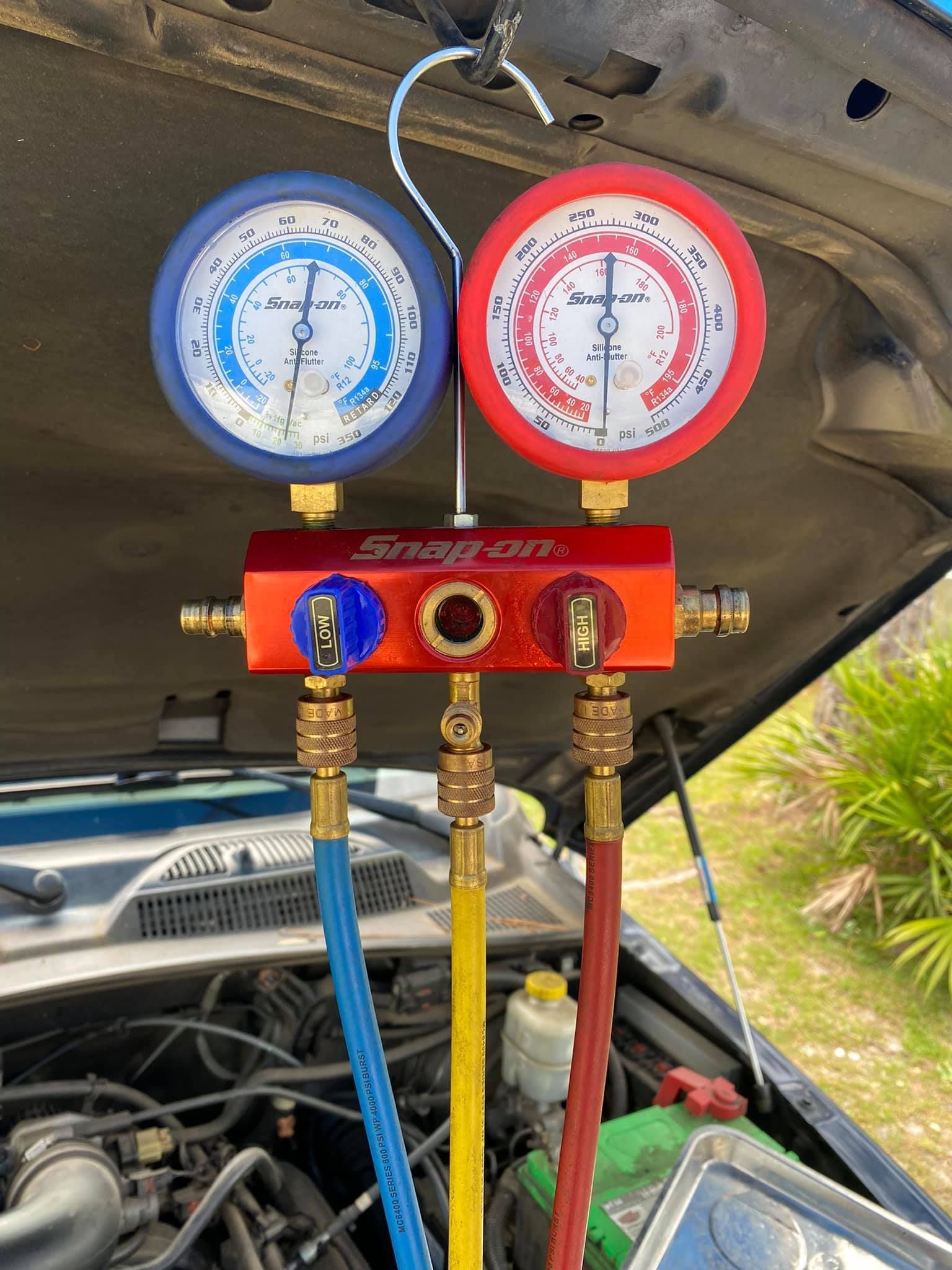 Close-up of car engine with Snap-on AC gauges: blue and red dials, attached hoses, hanging under the hood.